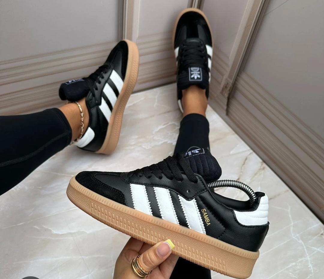 Tenis Adidas de inspiración Samba en negro con tres franjas blancas y suela caramelo.